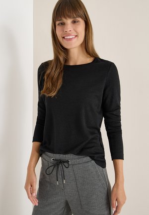 Haut noir à manches longues avec une texture lisse et un léger éclat, associé à un pantalon gris à motifs en chevron muni d'un cordon de serrage.