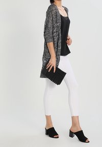 Svart och vit mönstrad kimono, svart linne, vita skinny jeans och svarta klackskor. Svart veckad clutch i handen.