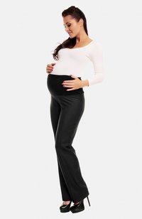 Pantalons de maternité noirs avec une ceinture large, associés à un haut ajusté à manches longues blanches, portés par une femme qui caresse doucement son ventre.