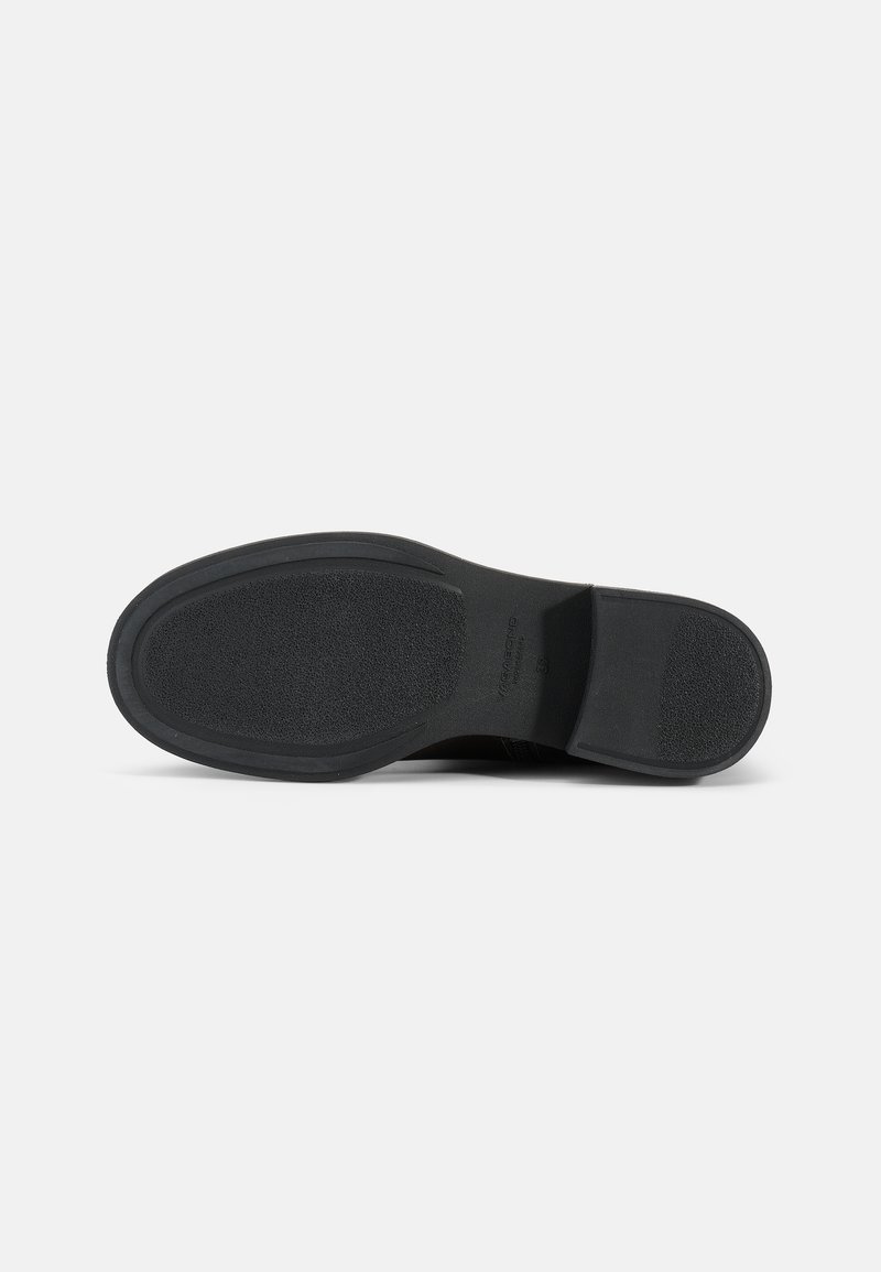 Semelle de chaussure noire avec une surface en caoutchouc texturée. Présente un design de bout et de talon lisse, une adhérence antidérapante et un détail de marque sur le côté.