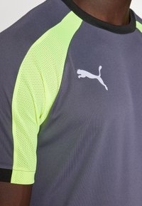 Grå athletisk skjorte med neongul mesh-detaljer på skuldrene, svart kant rundt kragen og hvit logo. Det er tydelig at stoffet har en fukttransporterende tekstur.