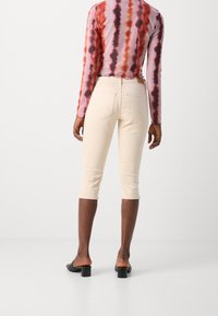 Knee-length béžové kalhoty s slim fit střihem, vyrobené z měkké tkaniny. Mají dvě zadní kapsy a štítek na pase. Nošeny s barevným tričkem s dlouhým rukávem.