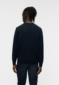 Σκούφο μπλε πουλόβερ με μακριά μανίκια, στρογγυλή λαιμόκοψη και ριμπ μανσέτες. Συνδυάζεται με σκούρο τζιν παντελόνι, ομαλή υφή, μίνιμαλ σχεδιασμός.