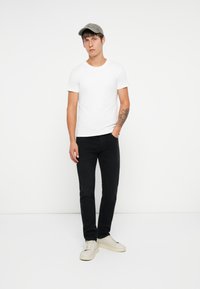T-shirt bianca a maniche corte, jeans neri, sneakers beige chiaro, cappellino da baseball grigio. Design semplice, silhouette aderente, senza motivi visibili.
