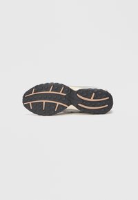 Suola di sneaker caratterizzata da un gomma nera testurizzata con impugnature circolari e dettagli in gomma marrone; porzione superiore grigia visibile.