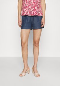 Shorts en denim bleu avec une coupe décontractée, ourlets retroussés, associés à un haut à motifs floraux rouges et des sandales à talons blocs nude.