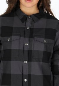 Camicia a quadri nera e grigia con colletto button-down, due tasche sul petto e bottoni in metallo argentato. Presenta un tessuto testurizzato.