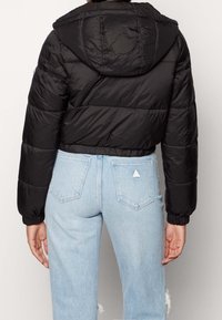 Czarna krótka kurtka puchowa z kapturem, o pikowanym fakturze i elastycznych mankietach, zestawiona z jasnoniebieskimi jeansami z wysokim stanem.