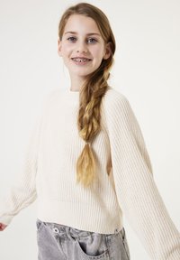 Lichtbeige gebreid sweater met een ribbelstructuur, ronde halslijn en verlaagde schouders, gedragen met grijze high-waisted broek.