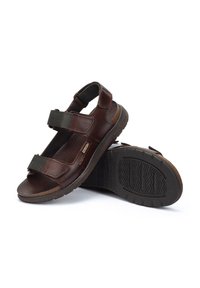 Sandalias de cuero marrón con correas ajustables de color verde oscuro, plantilla texturizada y suelas de goma con un patrón en zigzag para mayor agarre.