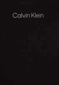 Textile noir avec le logo "Calvin Klein" en gris clair contrastant. Le tissu a une texture lisse avec un léger étirement.
