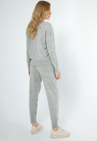 Grijze gebreide trui en bijpassende broek, met een relaxed fit. De stof heeft een zachte textuur en de outfit is gecombineerd met lichtgekleurde sneakers.