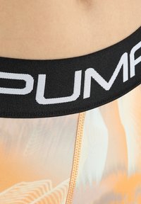Czarny elastyczny pas ze słowem "PUMA" wydrukowanym na białym tle, w połączeniu z szortami z gradientowym pomarańczowym wzorem i lekką siateczkową teksturą.
