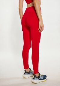 Rote Sportleggins aus dehnbarem Material, mit hohem Bund und schmaler Passform, kombiniert mit schwarz-gelben Sportschuhen.
