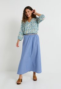 Blusa de estampado floral azul con cordones y mangas abullonadas, combinada con una falda maxi a rayas azules y blancas y sandalias de tacón cuadrado marrones.
