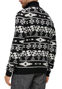 Schwarzer und weißer gemusterter Pullover mit hohem Kragen, der über geometrische Designs sowie gerippte Bündchen und Saum verfügt. Hergestellt aus Strickmaterial.