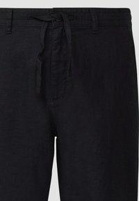 Pantalon noir avec passants de ceinture et cordon noué à la taille, avec une fermeture éclair dissimulée à l'avant.