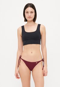 Black cropped bikini top with square neckline paired with burgundy ribbed tie-side bikini bottom featuring a small gold accent.