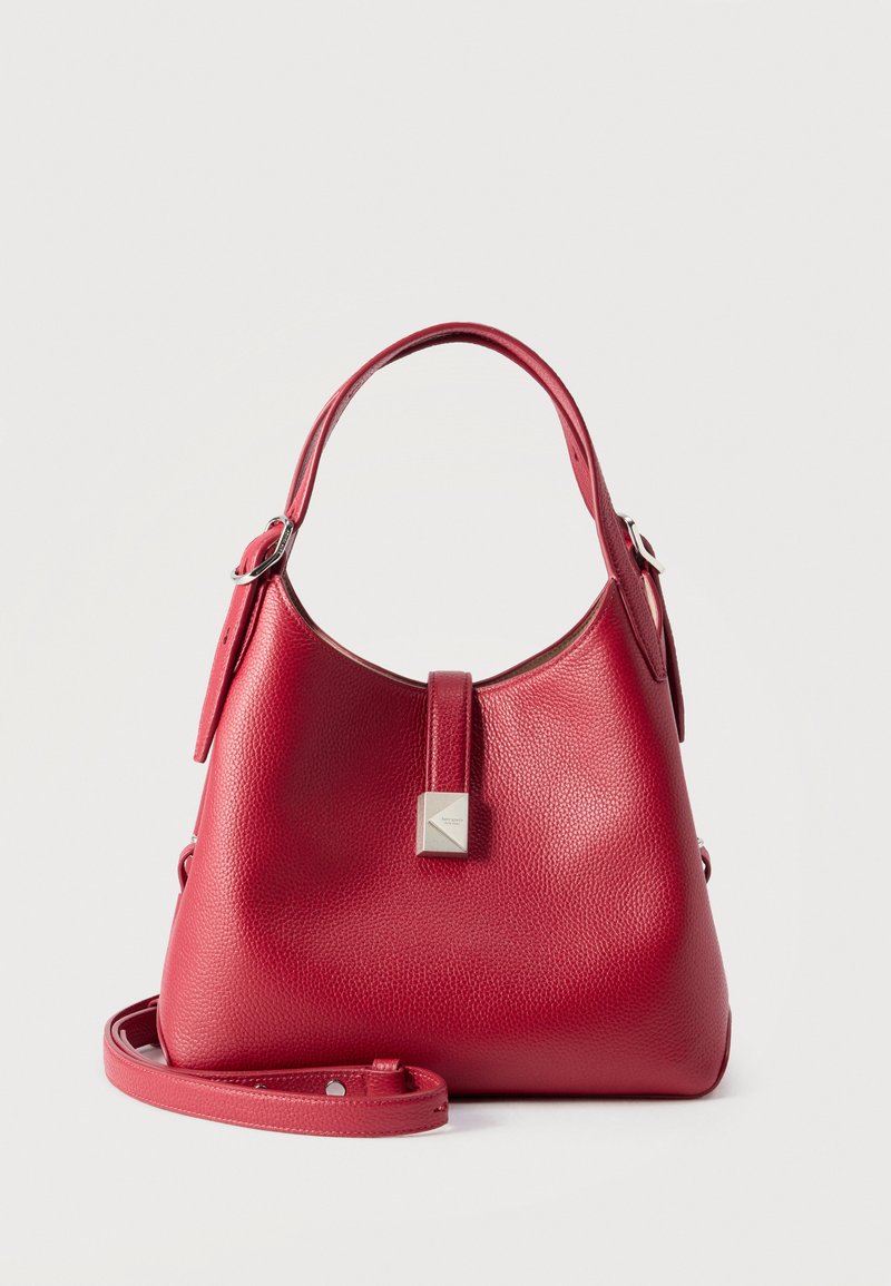 Κόκκινη δερμάτινη τσάντα με ανάγλυφη υφή, με ρυθμιζόμενα κοντά χερούλια, κούμπωμα με πατιλέτα, ασημένια τετράγωνη λεπτομέρεια και αποσπώμενο μακρύ λουράκι, σε ουδέτερο φόντο.