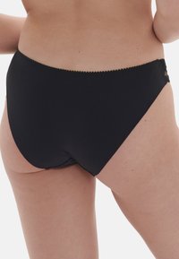 Parte inferiore del bikini nera realizzata in un materiale morbido e stretch, con un bordo in pizzo ondulato lungo la vita. Texture liscia e design a copertura totale.