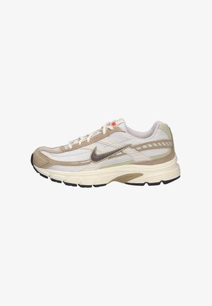 Beige Nike running shoe with mesh and suede upper, textured panels, white midsole, black outsole, and grey accents. Laces and logo in dark brown.