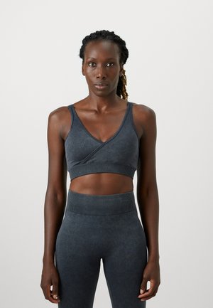 Soutien-gorge de sport extensible gris foncé avec un col en V et un design croisé ; bande côtelée en bas ; texture lisse, associé à un legging taille haute assorti.