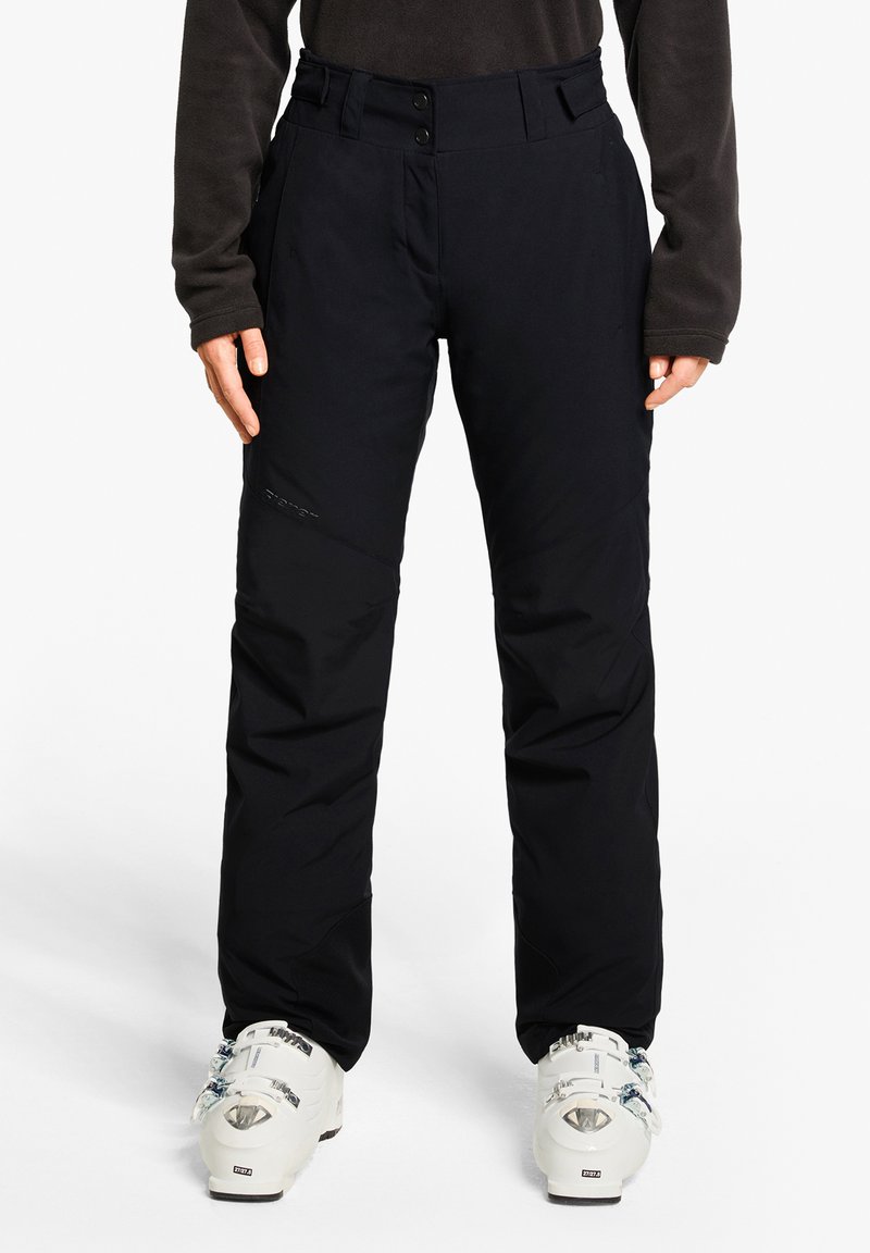 Black ski pants featuring a straight fit, two-button closure, and reinforced knee sections. Worn with white ski boots for contrast.