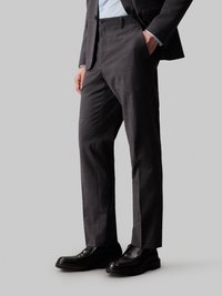 Dunkelgraue maßgeschneiderte Hose aus strukturiertem Stoff, mit flacher Vorderseite und seitlichen Taschen, kombiniert mit schwarzen Lederschuhen.