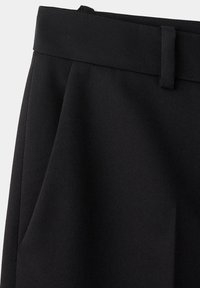 Gros plan sur un tissu noir montrant une ceinture avec passant pour ceinture et une poche latérale sur un pantalon sur mesure.
