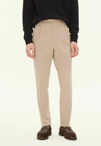 Beige, skräddarsydda byxor med flat front, enkel knappstängning och avsmalnande ben, kombinerat med mörka, strukturerade skor.