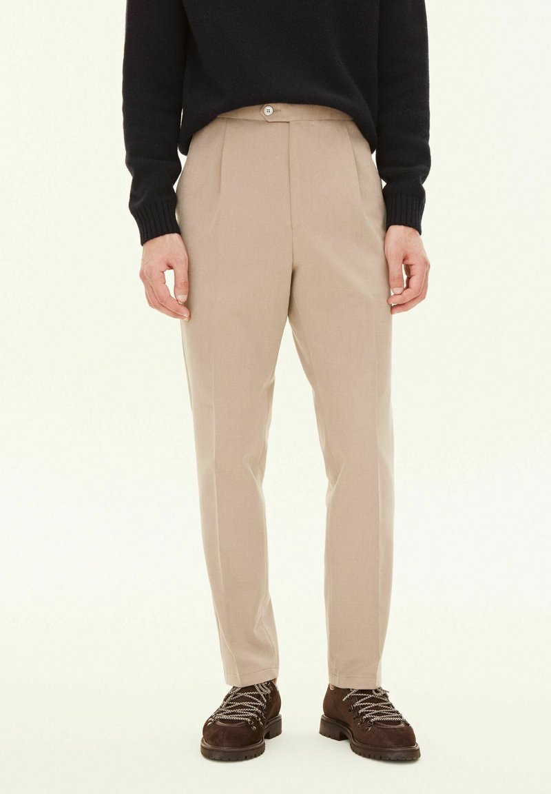Beige, skräddarsydda byxor med flat front, enkel knappstängning och avsmalnande ben, kombinerat med mörka, strukturerade skor.
