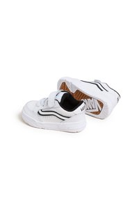 Sneakers bianchi con una striscia nera di accento, dotati di una fascia in Velcro, suole in gomma testurizzata e dettagli con fori lungo i lati.