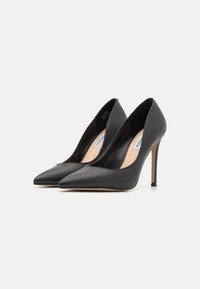 Sorte skinnhøye pumps med spiss tådesign, glatt tekstur og en slank stiletthæl. Fôret er nudefarget.