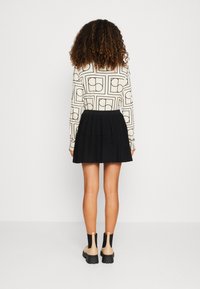 Långärmad blus i krämfärg med svarta geometriska mönster, kombinerad med en plisserad svart minikjol. Skorna är beige anklarboots med svarta sulor.