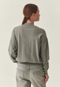 Pull gris à coupe décontractée, col et poignets côtelés. Associé à un jean en denim gris clair avec des poches arrière.