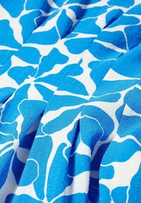 Tissu à motifs bleus et blancs avec des formes florales abstraites, présentant une surface texturée et des plis doux créant profondeur et mouvement.