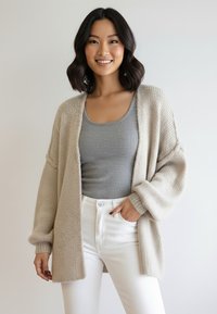 Beżowy kardigan z otwartym przodem o teksturowanym splocie, z oversize’owymi rękawami i miękkim wykończeniem. Połączony z dopasowanym szarym topem na ramiączkach i białymi dżinsami.