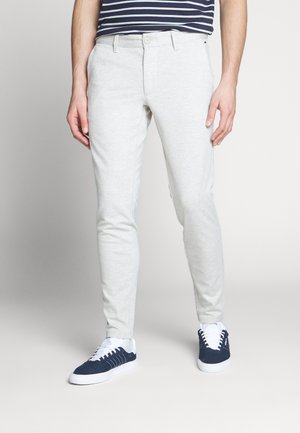 Lichtgrijze slim-fit broek van zachte stof, met een gladde textuur, twee voorzakken en een knoopsluiting. Gedragen met navy sneakers.