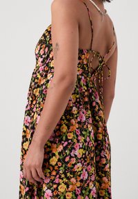 Blommig maxiklänning med svart bakgrund, prydd med rosa, orange och gula blommor; justerbara spaghetti-remmar och en knytning baktill.