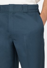 Pantalons navy avec une taille plate, des passants de ceinture et des poches latérales. Le tissu a une texture lisse avec un léger éclat.