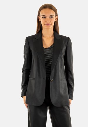 Blazer nero con design su misura, finitura in raso, revers a punta, chiusura con un solo bottone e due tasche frontali. Indossato sopra una maglietta a righe.