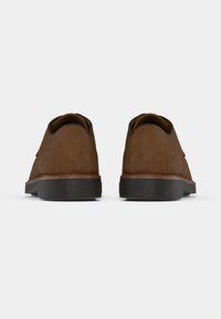 Chaussures en daim marron avec une texture lisse, conçues avec des bouts ronds et une semelle en caoutchouc noire contrastante. Design minimaliste sans ornements.