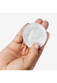 Rund, hvit bomullspad holdt i en hånd, lett fuktig med en glatt overflate, med en lys blå kant.