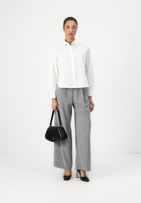 Camicia bianca con righe verticali, pantaloni larghi grigi, borsa nera e tacchi a punta neri. Design minimalista e linee pulite.