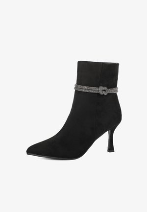 Stivale alla caviglia in suede nero con punta affusolata e tacco sottile. Presenta una banda decorativa intrecciata in tonalità argento attorno alla parte superiore. Texture liscia.