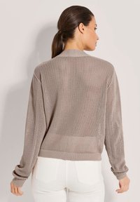 Leichter, beiger Mesh-Pullover mit langen Ärmeln, gerippten Bündchen und lockerer Passform. Verfügt über ein strukturiertes Muster mit einem verkürzten Rücken.