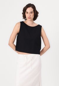 Svart kort ermeløs topp med bred rund hals, laget av glatt stoff, kombinert med en hvit bukse med snor. Enkelt design.