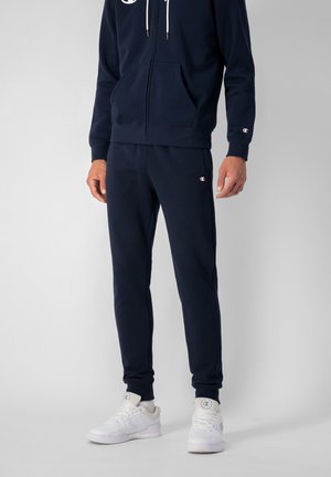 Felpa con zip colore blu navy, dotata di tasche frontali, stringhe bianche, pantaloni abbinati e dettagli bianchi sulle sneakers. Tessuto morbido con dettagli del logo.