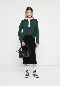 Grön långärmad tröja med vit krage, svart knälång kjol, svart handväska, vita strumpor och svarta sneakers med vita detaljer.