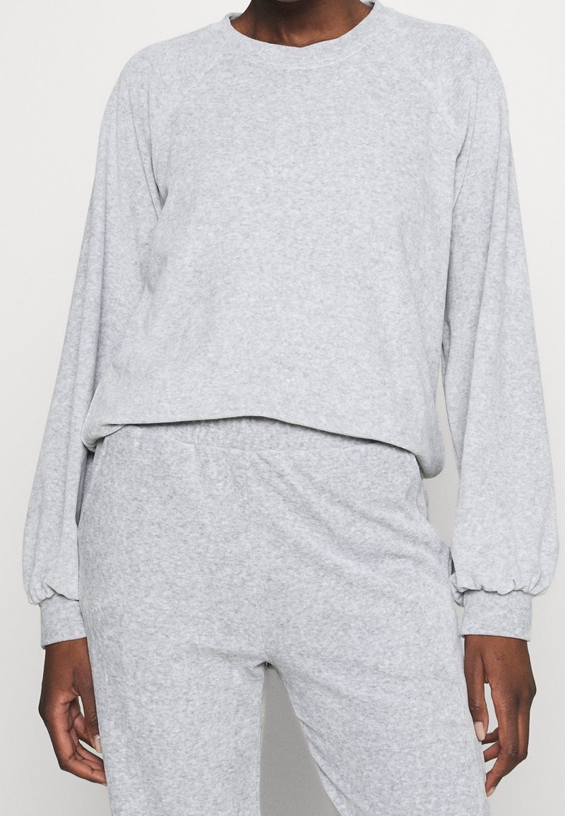 Sudadera de tela suave de color gris claro con mangas largas raglán, cuello redondo y un ajuste holgado. Pantalones deportivos a juego visibles en la cintura.